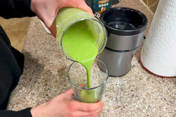Ruky nalievajú zelené smoothie zo šálky kompaktného osobného mixéra Ninja BN301 Nutri-Blender Plus do pohára na pitie