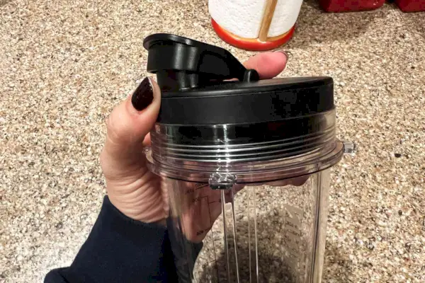 Ruka držiaca cestovné viečko a šálku kompaktného osobného mixéra Ninja BN301 Nutri-Blender Plus