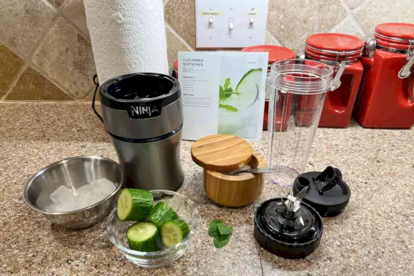 Kompaktný osobný mixér Ninja BN301 Nutri-Blender Plus s nakrájanou uhorkou a kockami ľadu v miskách na kuchynskej linke