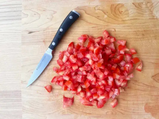 Wusthof Classic Ikon Paring Knife는 나무 테이블 위의 다진 토마토 근처에 표시됩니다.