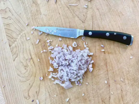 Wusthof Classic Ikon Paring Knife는 나무 테이블 위의 다진 양파 근처에 표시됩니다.