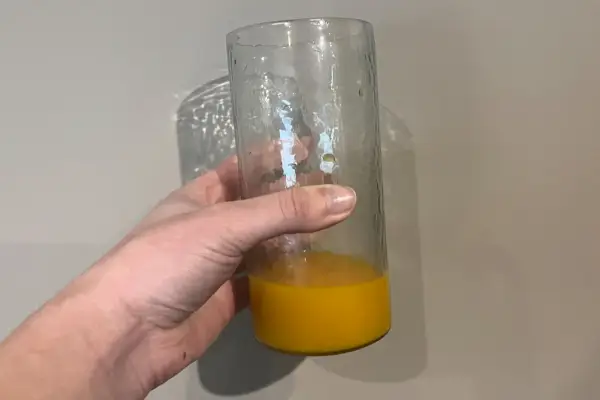 Una persona tiene in mano un bicchiere di succo d'arancia martellato alto realizzato a mano da Pottery Barn