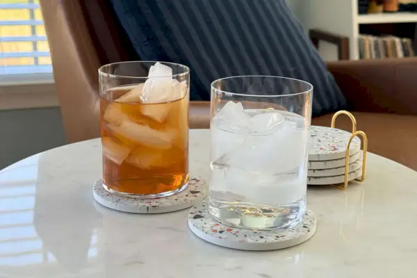 Due bicchieri Made In pieni di ghiaccio e liquidi siedono sui sottobicchieri su un tavolo di marmo