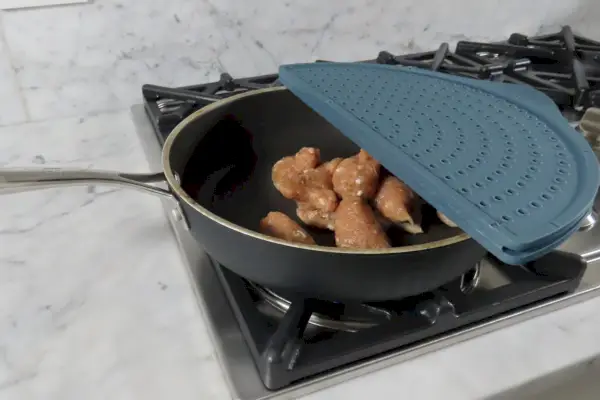 Der Silikon-Spritzschutz von Williams Sonoma deckt ein in der Pfanne gebratenes Hähnchen ab