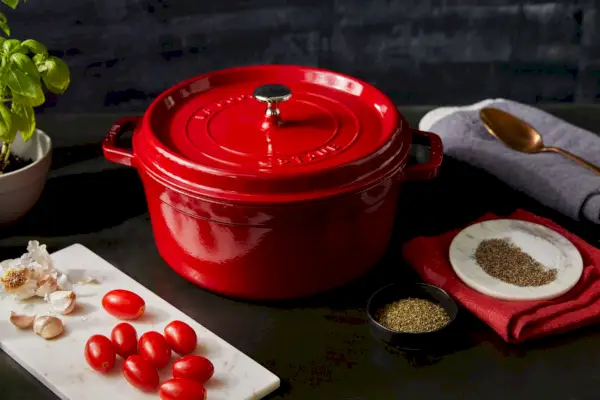 Staub 5,5 Quart Round Cocotte auf dem Tisch neben Tomaten, Knoblauch und Gewürzen
