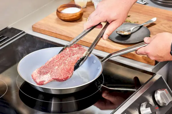 Eine Person kocht Fleisch in der beschichteten Pfanne