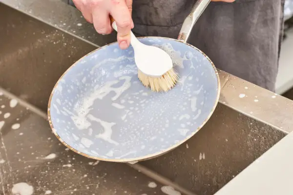 Eine Person wäscht das Material der beschichteten Pfanne in einem Waschbecken