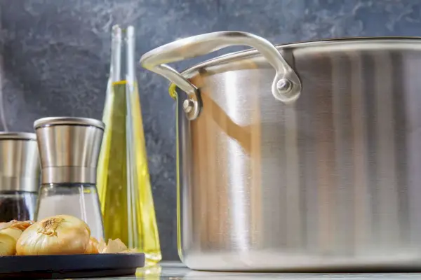 Nahaufnahme eines beschichteten Suppentopfs „Made In“ mit Salz- und Pfefferstreuer, einer Flasche Öl und kleinen Zwiebeln