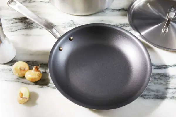 Hergestellt in einer beschichteten Bratpfanne und Deckel auf einer Marmorarbeitsplatte mit kleinen Zwiebeln