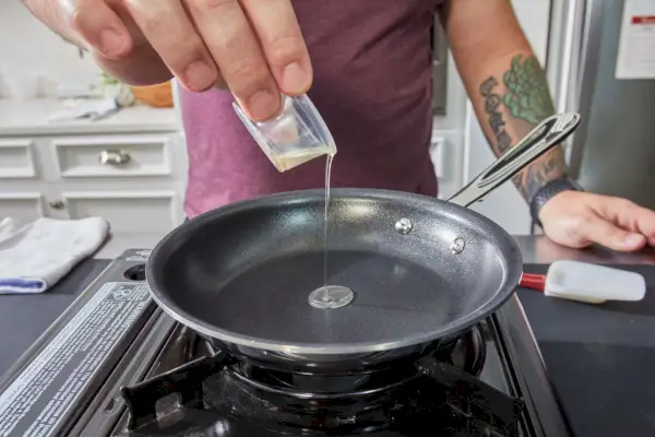 Öl wird in die All-Clad D3 Stainless Steel Tri-Ply Bonded 10-Piece Antihaft-Kochgeschirr-Pfanne gegossen