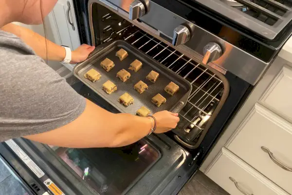 Person legt ein antihaftbeschichtetes Backblech von Circulon Total Bakeware mit Keksteig in den Ofen