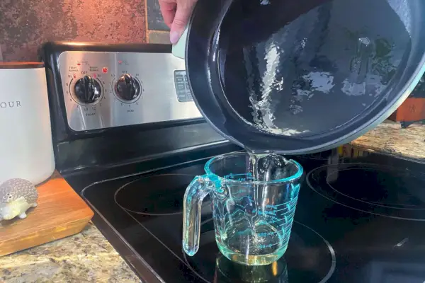 Eine Hand gießt Öl aus der emaillierten Gusseisenpfanne/Pfanne von KitchenAid in einen Messbecher