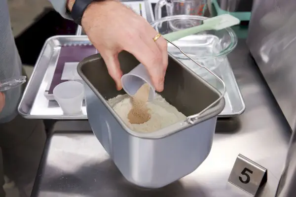 内部のバケツに材料を手で注ぎます。 ステンレス製のカウンターに展示された Breville カスタム ローフ ブレッド メーカー