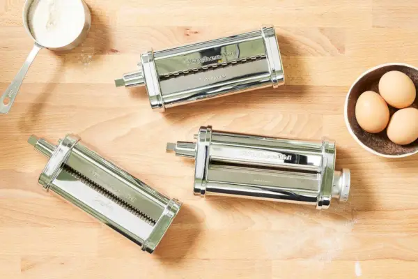 3-dielna súprava nástavca na valček na cestoviny a krájač KitchenAid zobrazená na drevenom povrchu s múkou a vajcami
