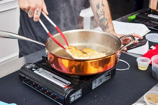 Eine Person kocht Hühnchen im 10-teiligen Williams Sonoma Thermo-Clad Copper Kochgeschirrset