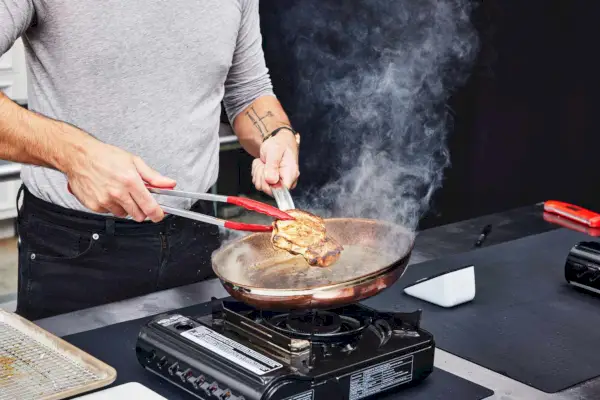 Eine Person kocht Fleisch in der Pfanne des Hestan CopperBond 10-teiligen Kochgeschirr-Sets