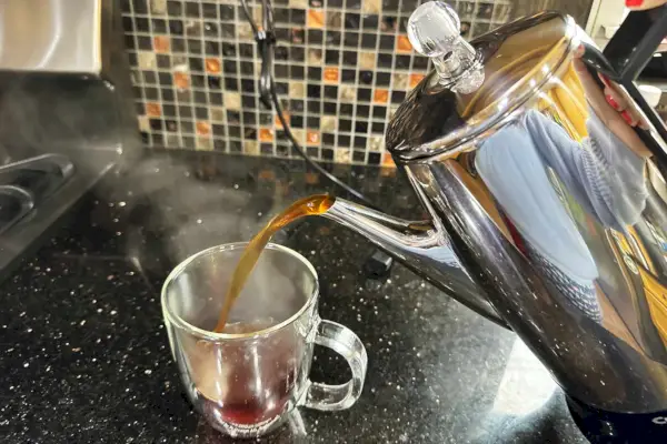 Osoba si nalévá kávu z nerezového perkolátoru Cuisinart Classic na 12 šálků do sklenice