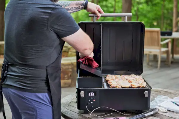 Traeger TFB30KLF Tailgater Pellet Grill에 닭 날개를 얹고 있는 사람