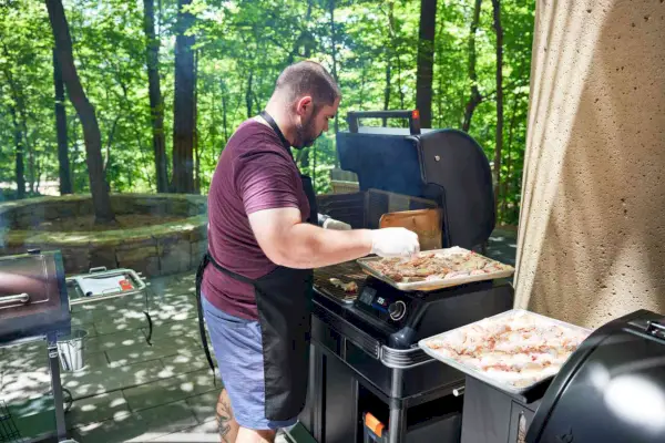Traeger TBB86RLG Timberline Pellet Grill에 닭날개를 올리고 있는 사람