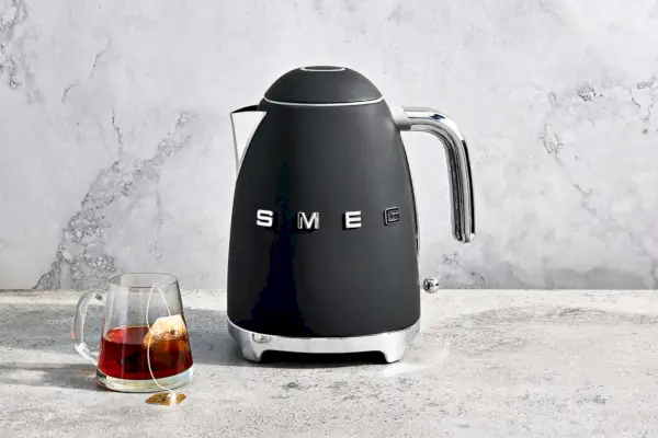 Czajnik elektryczny Smeg wystawiony na marmurowym blacie obok szklanego kubka z torebką herbaty w środku