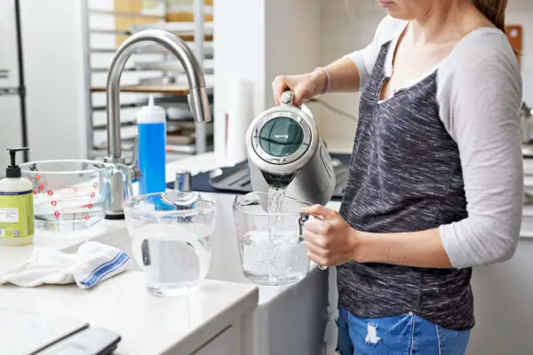 Osoba nalewająca wodę do miarki z Breville Smart Kettle Luxe przy pobliskim zlewie kuchennym