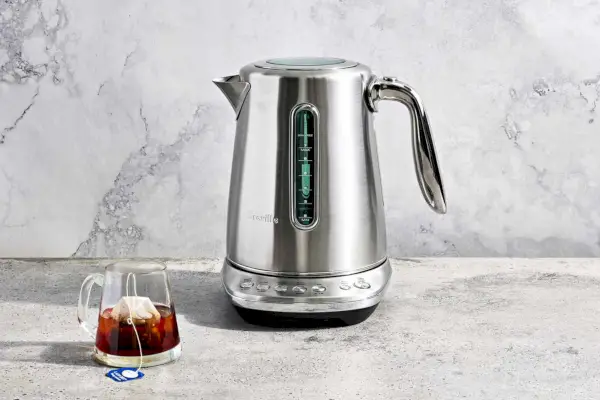 Breville Smart Kettle Luxe wystawiony na marmurowym blacie obok szklanego kubka z torebką herbaty w środku
