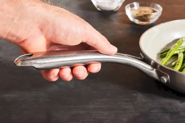 Eine Person hält den Griff der 10-teiligen GreenLife Stainless Pro Kochgeschirr-Pfanne