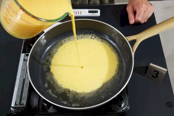 Eier werden in die Pfanne des 10-teiligen GreenPan GP5 Edelstahl-Kochgeschirrsets gegossen