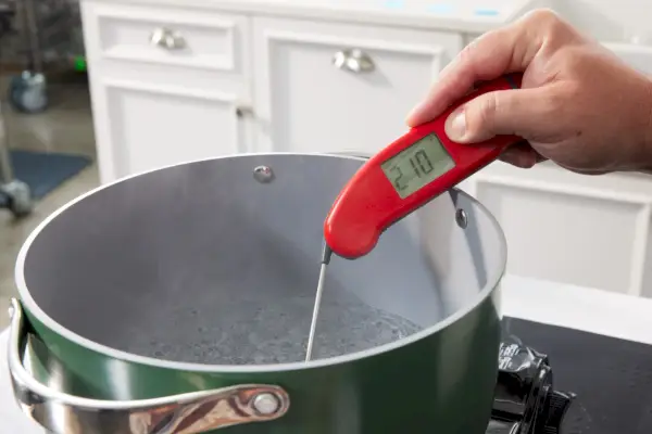 Eine Person misst die Temperatur des Wassers in der Pfanne des Caraway Antihaft-Keramik-Kochgeschirrsets
