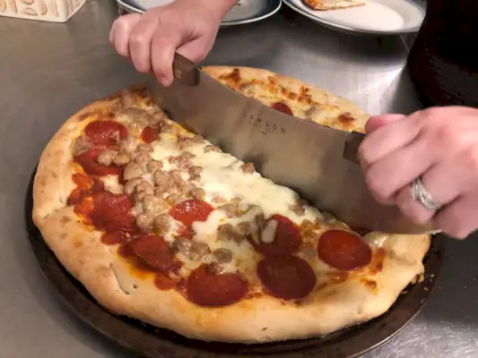 אדם שמשתמש ב-Lamson Pizza Rocker כדי לחתוך פיצה