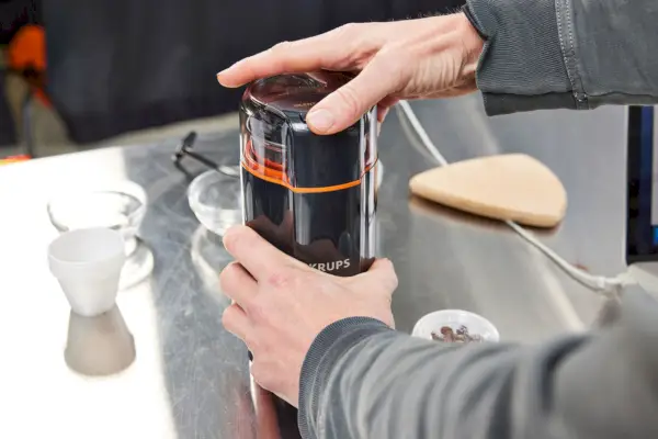 osoba držící elektrický mlýnek KRUPS Silent Vortex na nerezovém pultu