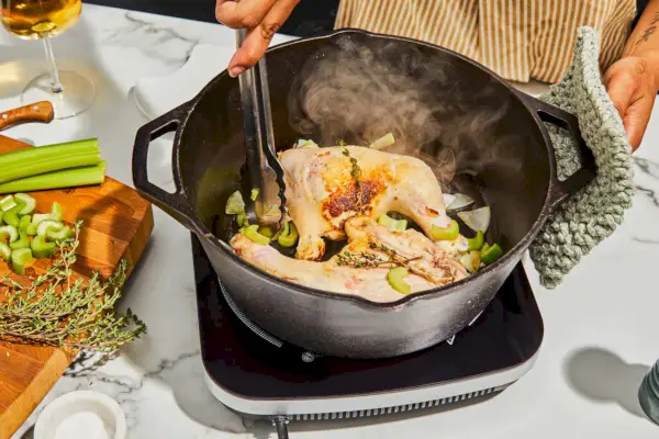 Eine Person kocht Hühnchen im 5-Quart Gusseisen-Doppel-Dutch-Ofen der Lodge