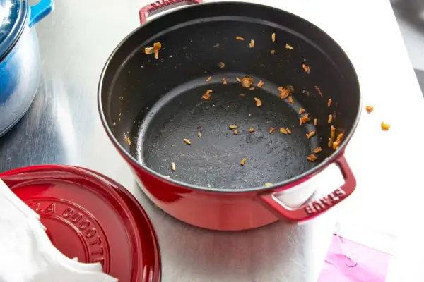 Eine Person öffnet den Deckel der runden 5,5-Quart-Cocotte aus Gusseisen von Staub