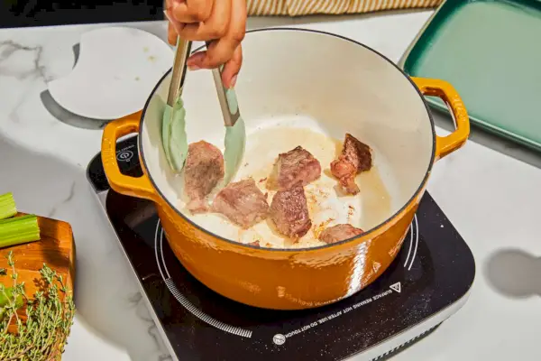 Eine Person, die Fleisch im emaillierten 5,5-Quart-Schmortopf aus emailliertem Gusseisen von Milo by Kana anbraten