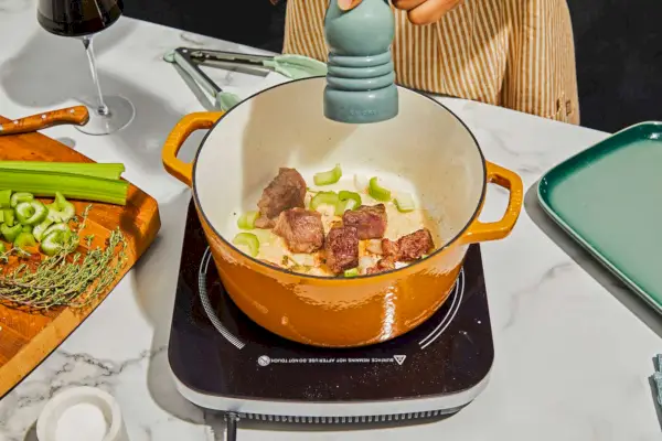 Eine Person würzt Fleisch im 5,5-Liter-Schmortopf aus emailliertem Gusseisen von Milo by Kana