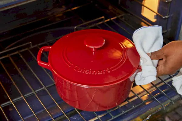 Eine Nahaufnahme einer Person, die die gusseiserne 5,5-Quart-Rundcocotte von Staub mit Ofenhandschuhen hält