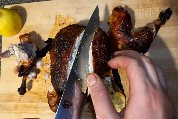 Una persona que usa el cuchillo Shun DM-0720 Classic de 9 pulgadas para cortar un pollo