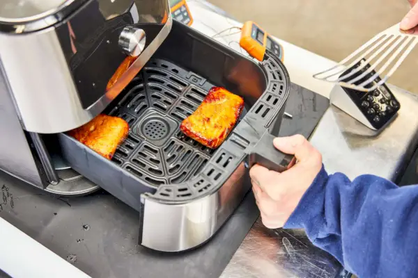 Mano sosteniendo la canasta de la freidora de aire 6 en 1 Instant Pot Vortex Plus de 6 cuartos con carne cocida
