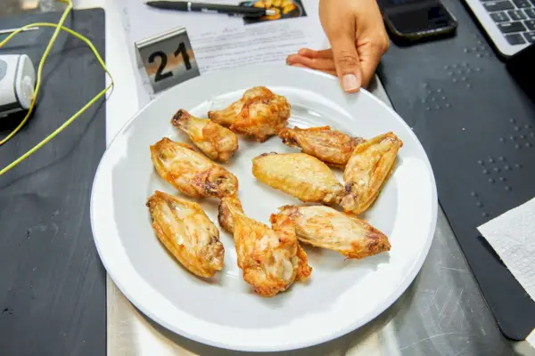 Mano sosteniendo un plato de alitas de pollo cocidas
