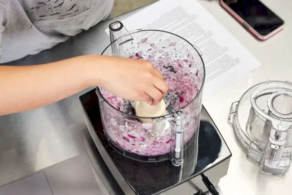 Mão levantando a lâmina de um Cuisinart cheio de cebola picada
