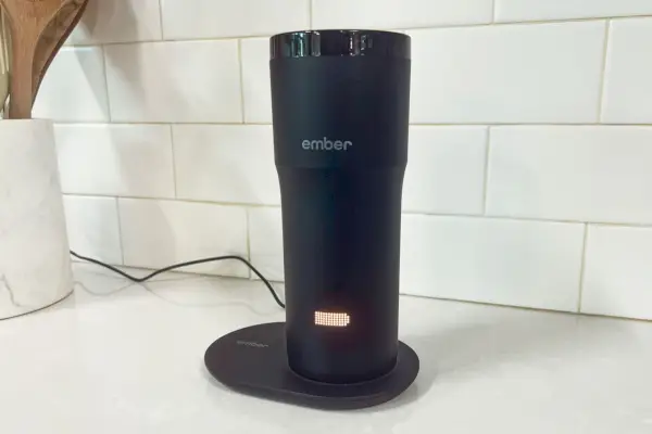 Čierny cestovný hrnček Ember Travel Mug sa nabíja na kuchynskej doske.